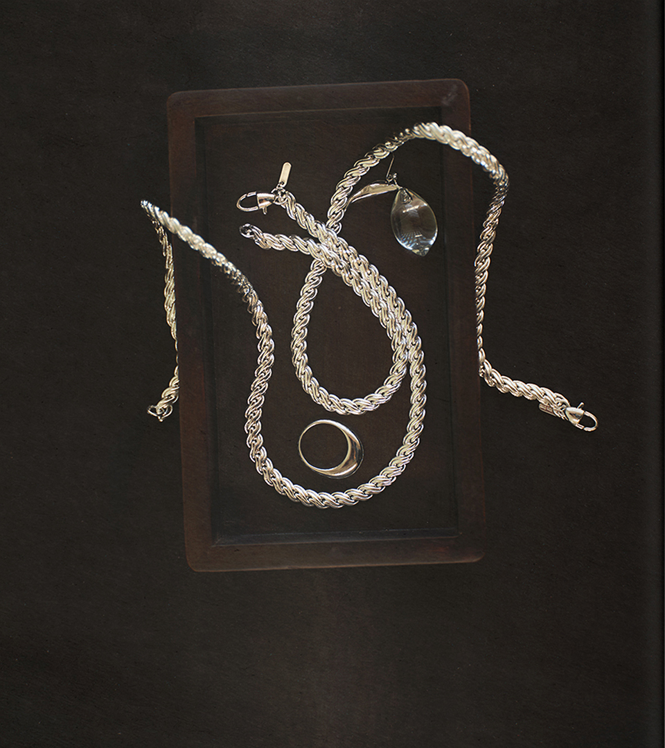 Composition of silver chain-link necklaces, rings and pendant on a dark surface
