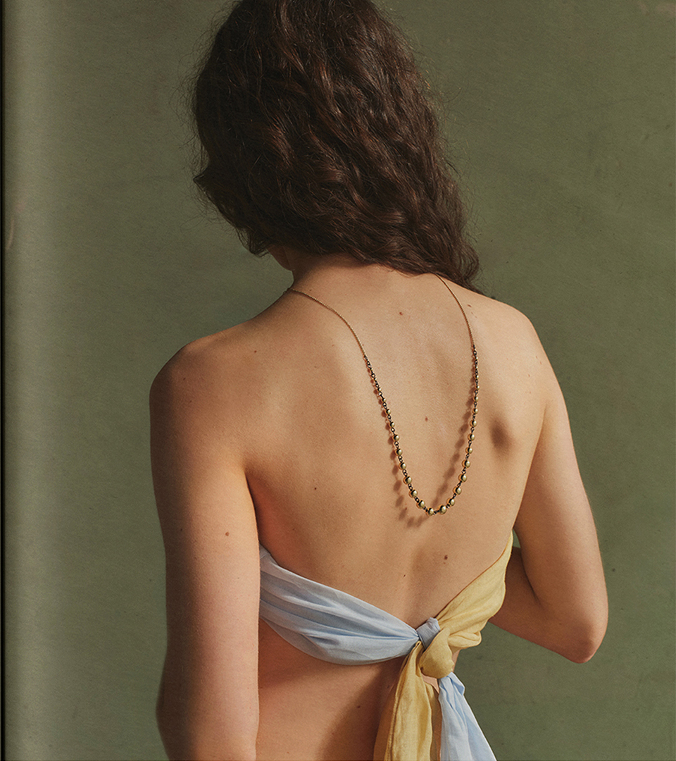 Model seen from behind wearing a silver chain-link necklace and plain linen scarf