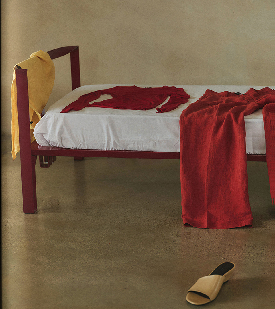 Bed with red clothing and leather mule on concrete floor