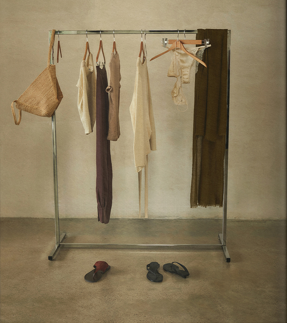 Metal clothes rack with garments in neutral and earthy tones, raffia bag and sandals on the floor