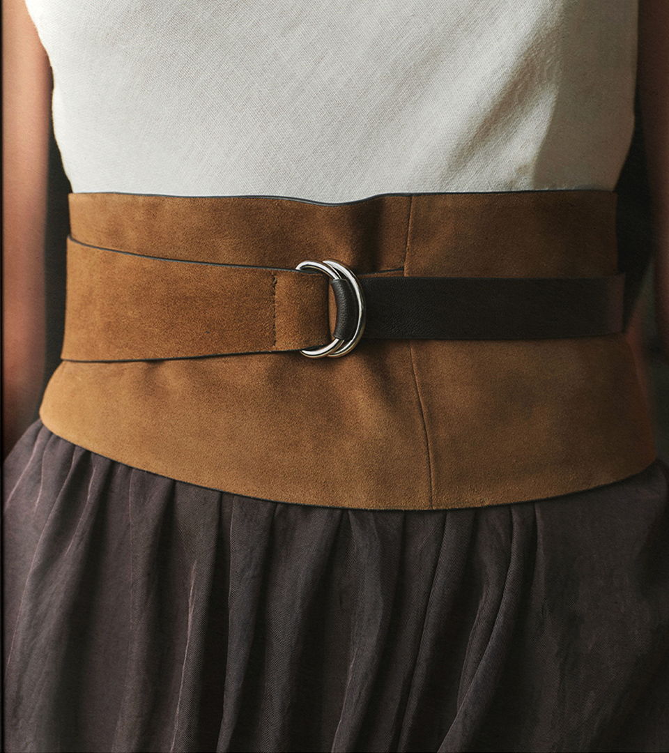 Close-up detail of a wide belt with oval buckle in brown suede over a pleated skirt