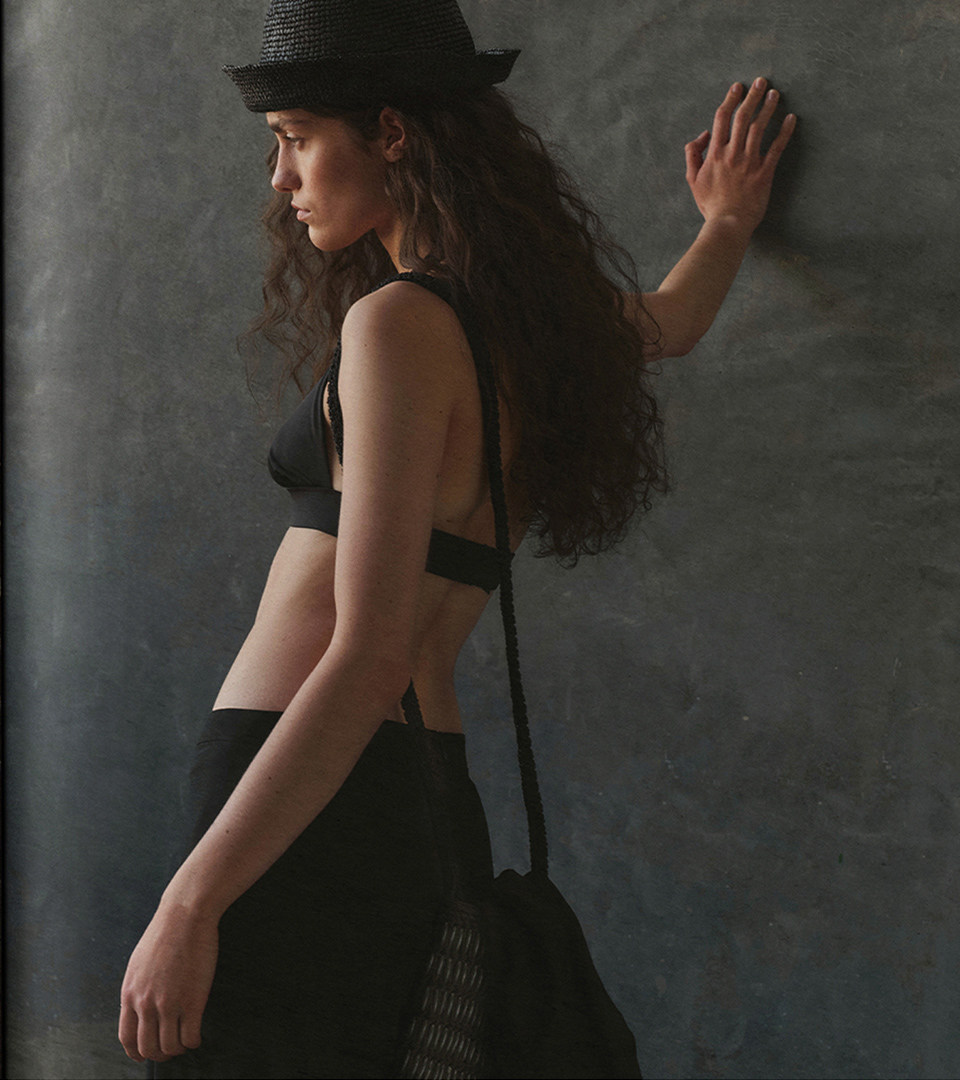 Model wearing a raffia bucket hat, black top and wooden-piece crossbody bag