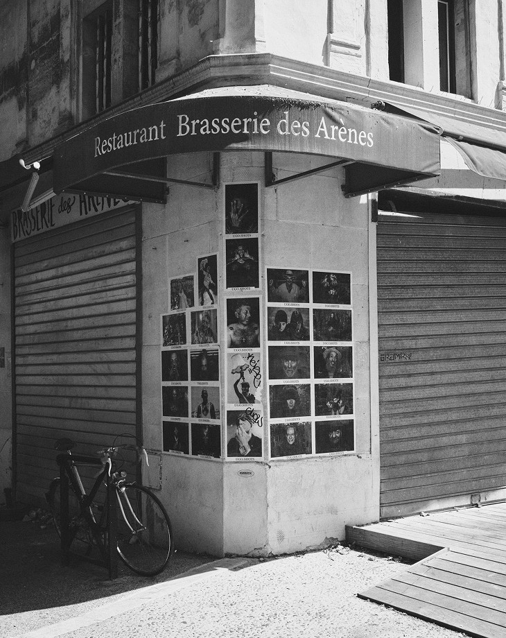 Façade of the Brasserie des Arènes with photographs in the window, in black and white — Arles
