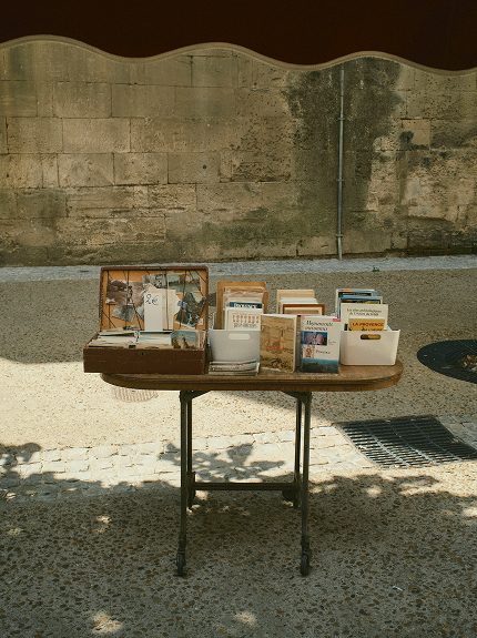 Table of photography books in the street, beside a wall — Arles