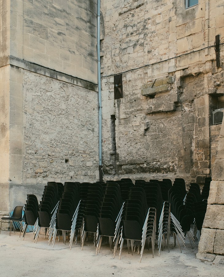 Chairs stacked against a pale stone wall — Arles