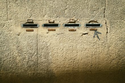 Four metal letterboxes on a sunlit stone wall — Arles