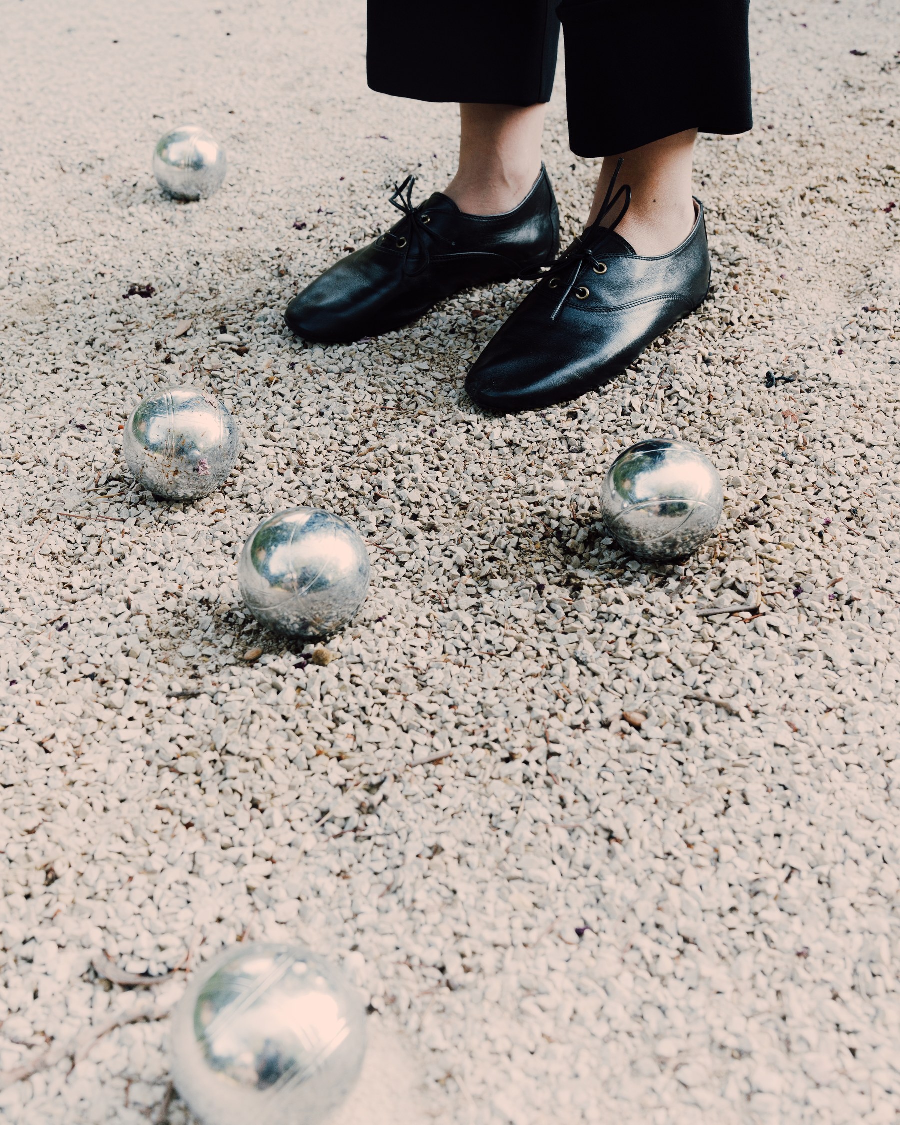 Black leather lace-up shoes on gravel next to pétanque balls — Massimo Dutti Fall Treasures