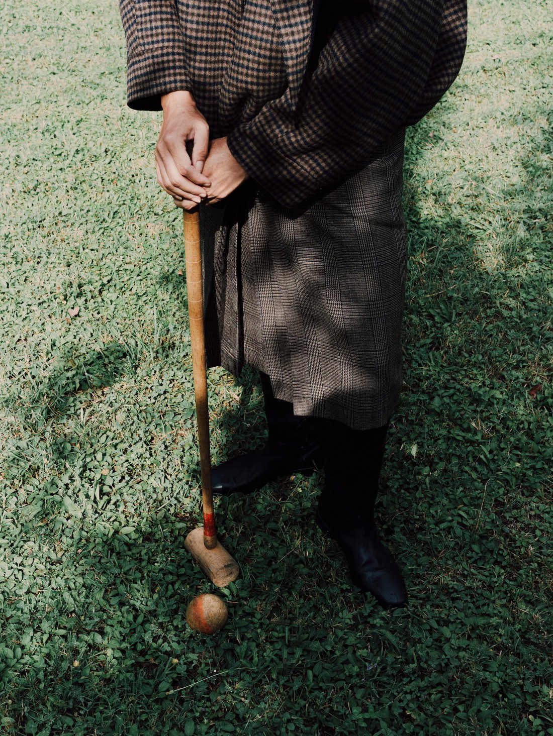 Hands resting on a croquet mallet on the grass, checked coat — Massimo Dutti Fall Treasures