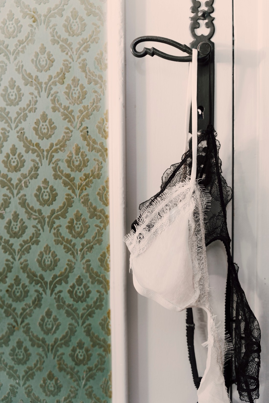 White bralette and black lace bra hanging from a hook next to wallpaper — Massimo Dutti Fall Treasures
