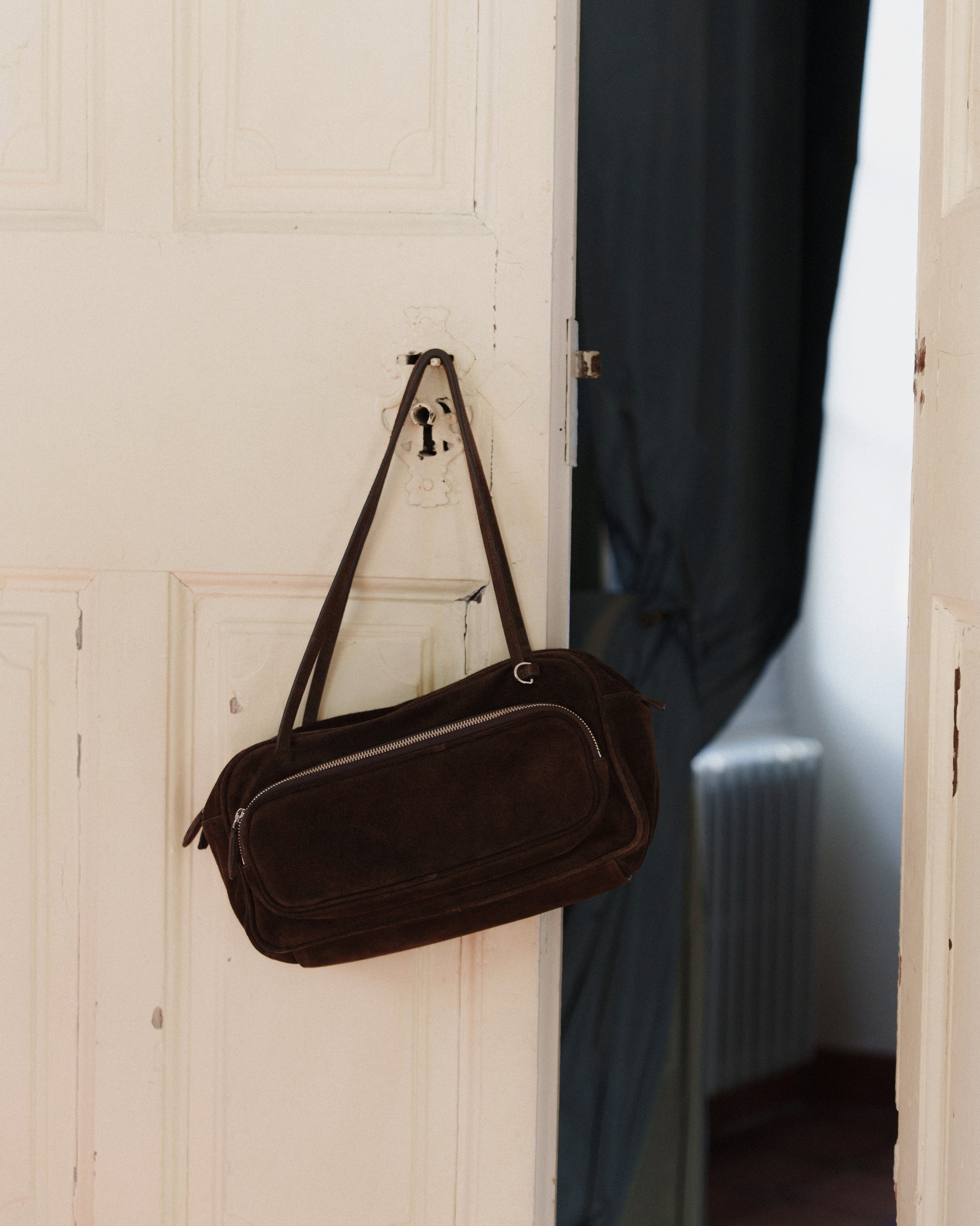 Suede bowling bag hanging from a white door — Massimo Dutti Fall Treasures