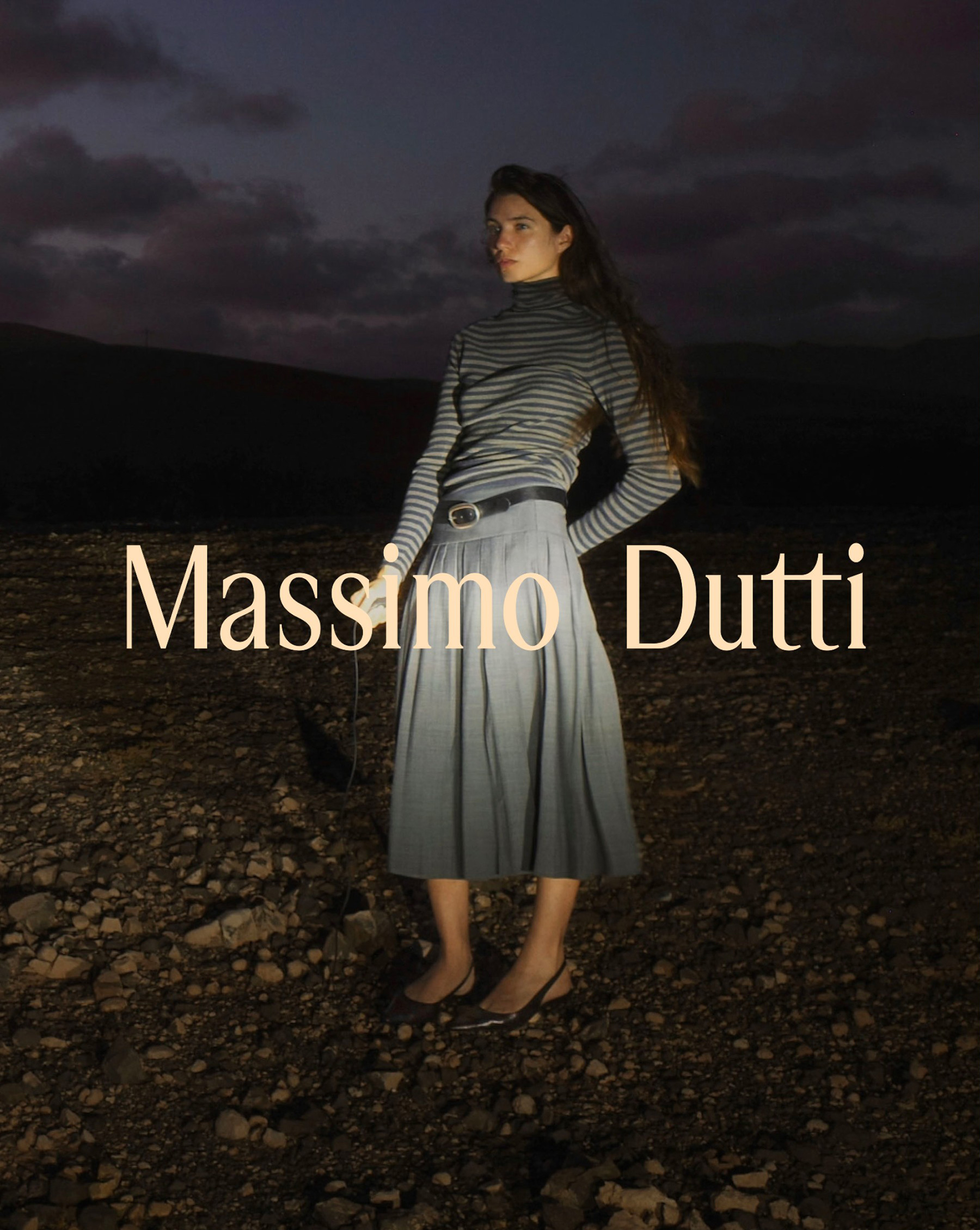 Model in a striped sweater and pleated midi skirt in a volcanic landscape at dusk, Fuerteventura — Massimo Dutti