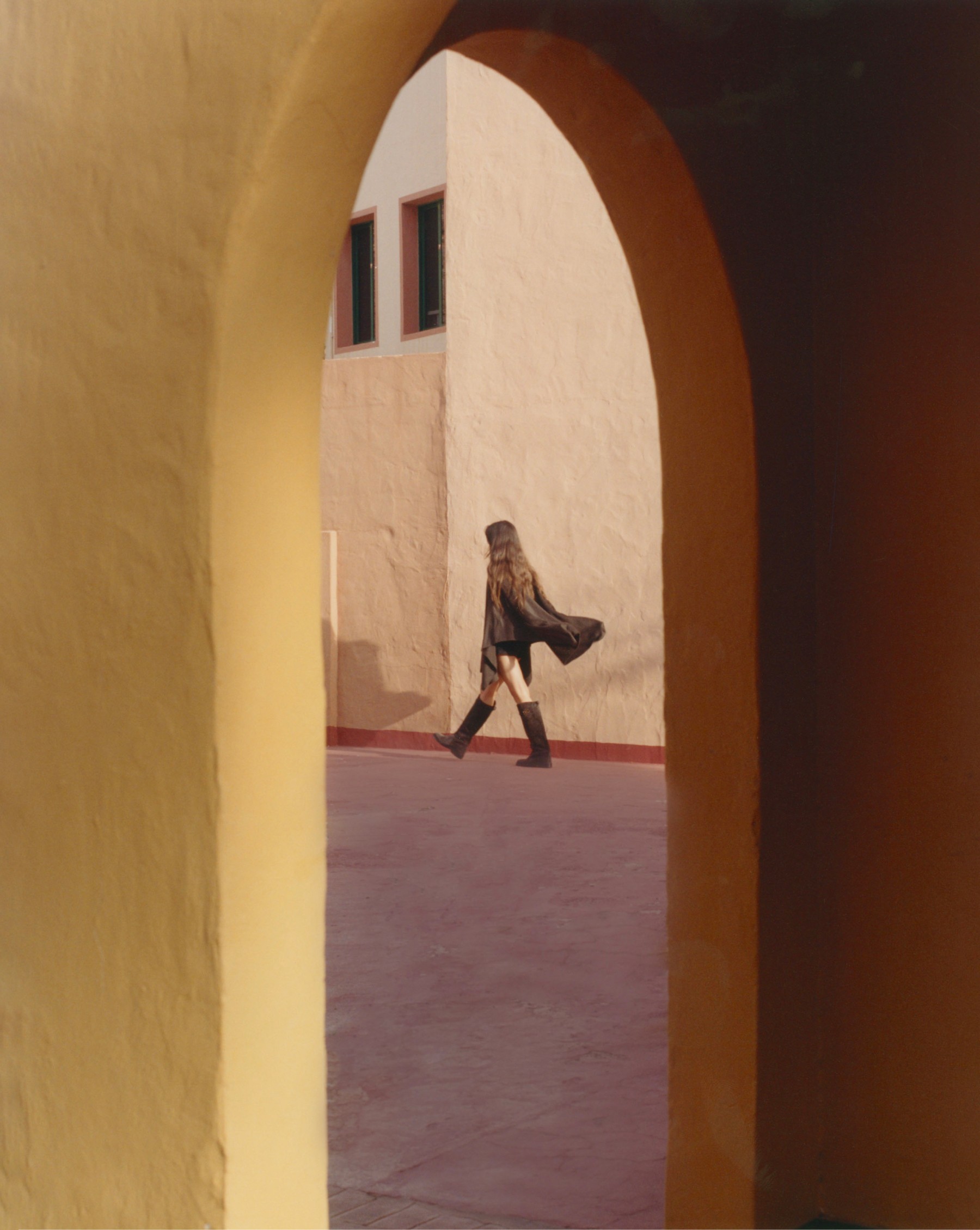 Model walking beneath an arch of ochre walls, Fuerteventura — Massimo Dutti