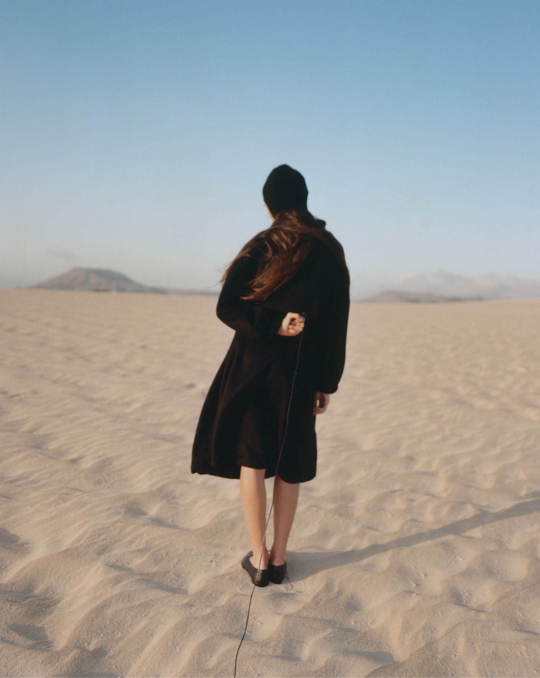 Model from behind in a black coat on the Corralejo dunes, Fuerteventura — Massimo Dutti