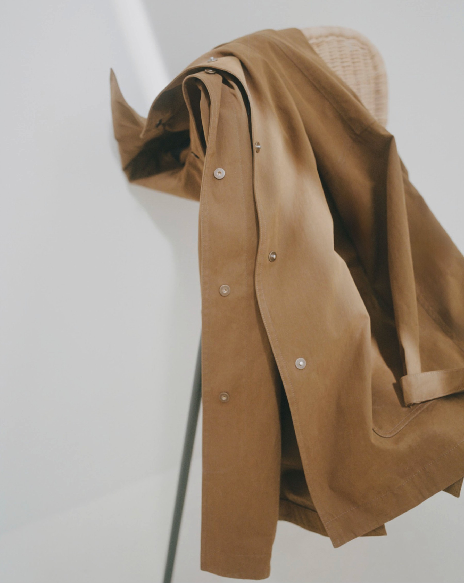 Camel trench coat hanging from a rush chair against a white wall — Massimo Dutti
