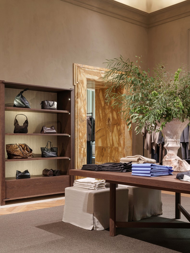 Handbag shelving beside a marble doorframe and a table with folded garments — Massimo Dutti Rome