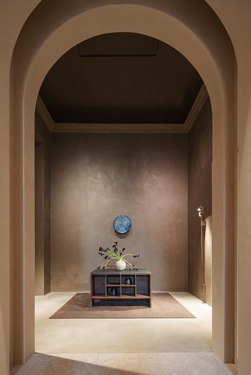 Entrance hall with an arch, stucco walls and a wooden sideboard beneath a medallion — Massimo Dutti Rome