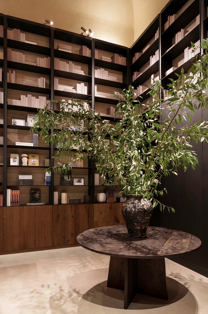 Bookshop with floor-to-ceiling shelves, a round stone table and an olive tree — Massimo Dutti Rome