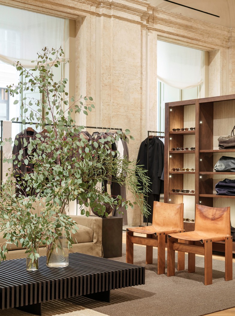 Green branches on a low table beside leather chairs and accessory shelving — Massimo Dutti Rome