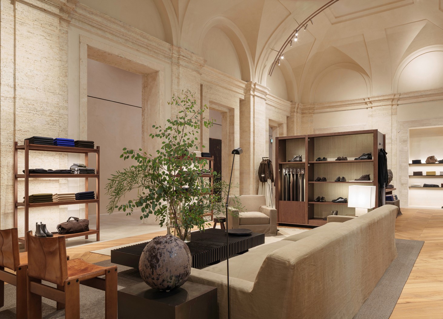 Menswear room with a sofa, coffee table, plant and shelving beneath the vaults — Massimo Dutti Rome