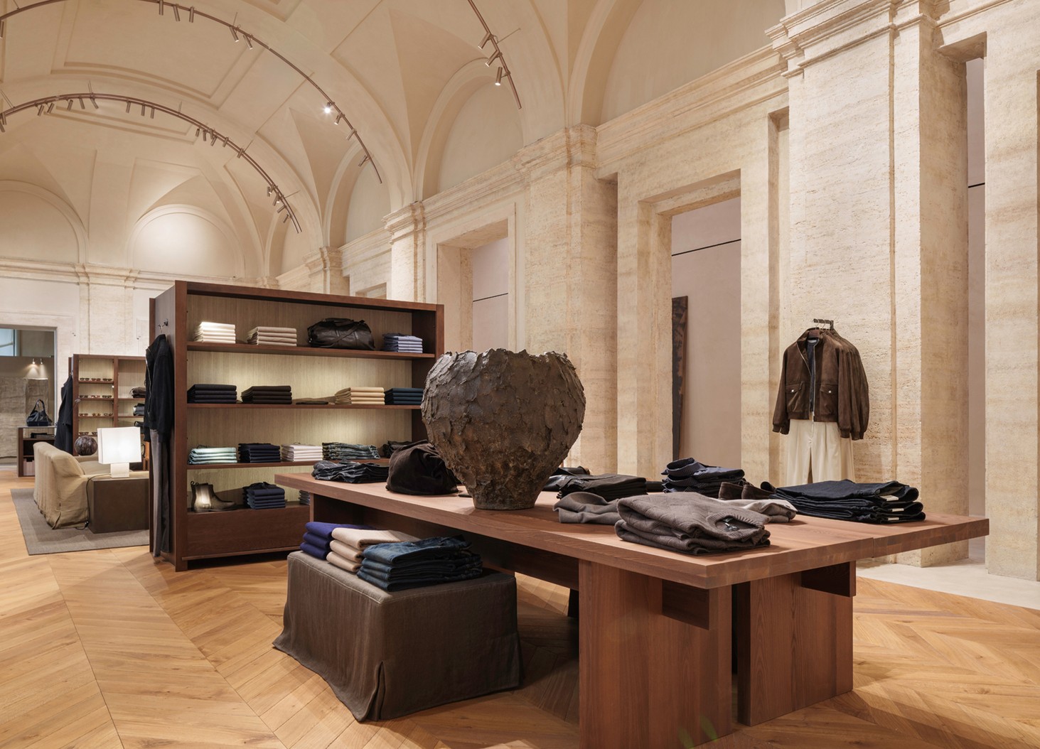Wooden table with folded menswear and a ceramic piece beneath the vaults — Massimo Dutti Rome