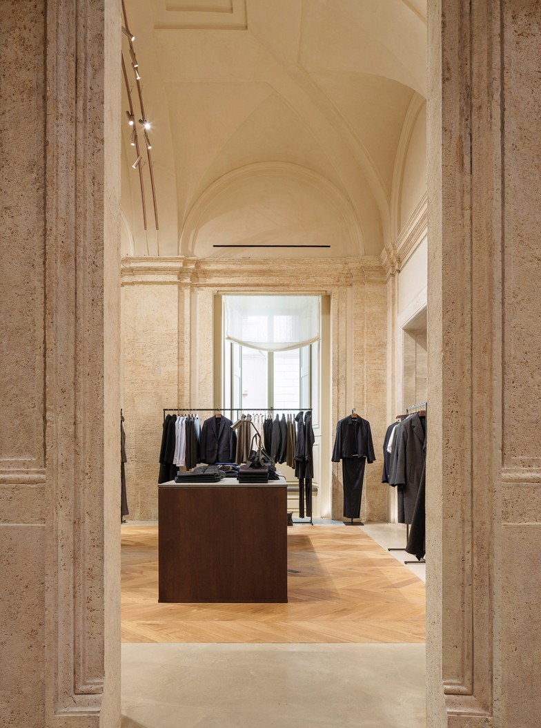 Travertine opening into the menswear room with clothing rails and a table — Massimo Dutti Rome